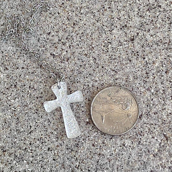 Waterproof silver dichroic glass cross necklace on sand with coin for scale