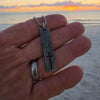Stainless steel cross bar necklace for men on a box chain held in the hand at a beach sunset, waterproof surfer cross