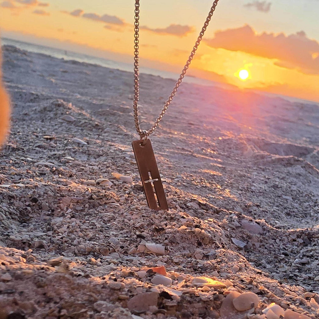 Cutout cross bar necklace on a stainless steel box chain set in beach sand at sunset, waterproof cross necklace for men