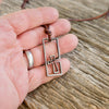 Men's cross necklace held in the hand to show size, handmade stainless steel surfer cross pendant on a leather cord