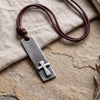Stainless steel cross bar necklace for men with coiled reddish-brown leather cord on linen and stone, Christian beach jewelry