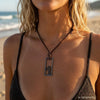Woman on the beach wearing a stainless steel surfer cross necklace on a leather cord, unisex Christian cross for men and women